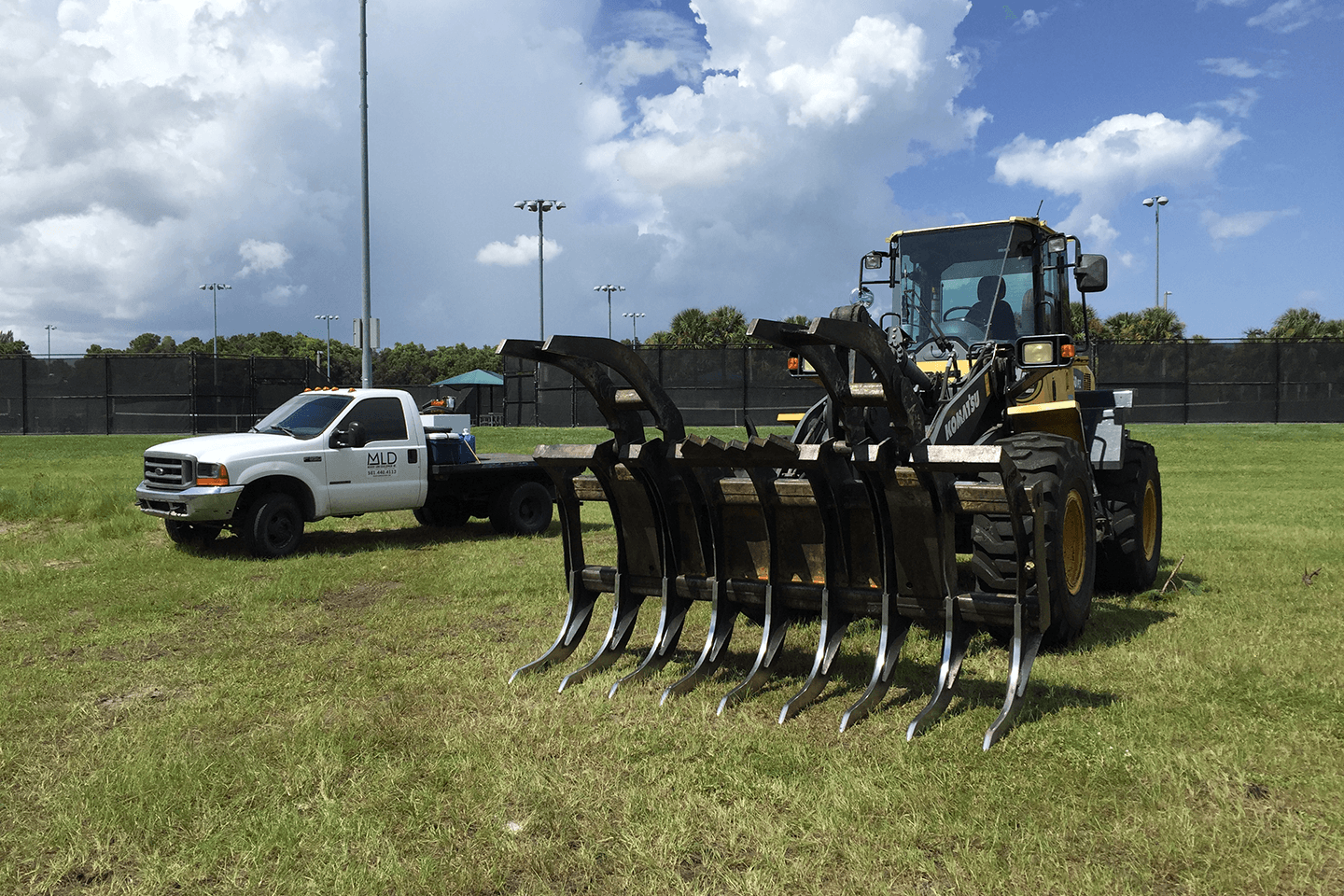 Pickup truck and front end loader in a grassy field
